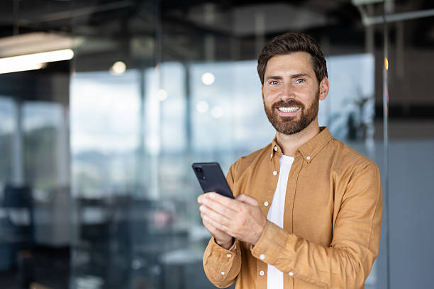 istock Confident man in modern office using smartphone and smiling at the camera 2245499317