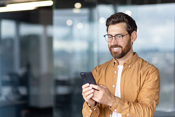 istock A man with glasses smiles while looking at his phone in an office environment. 2245499319