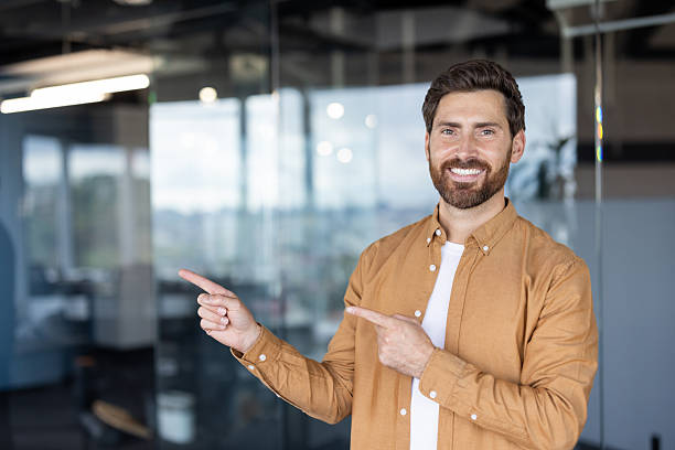 istock A happy man with a beard is pointing with both hands and smiling, looking confident. 2245499328