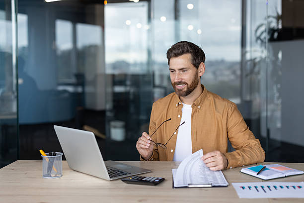 istock A businessman reviews documents at his desk in a modern office, smiling and working. 2245499413