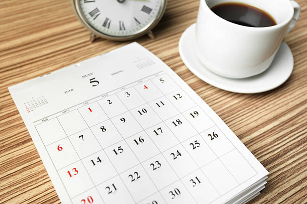 Coffee cup and clock next to a calendar on a wooden table in a morning setting