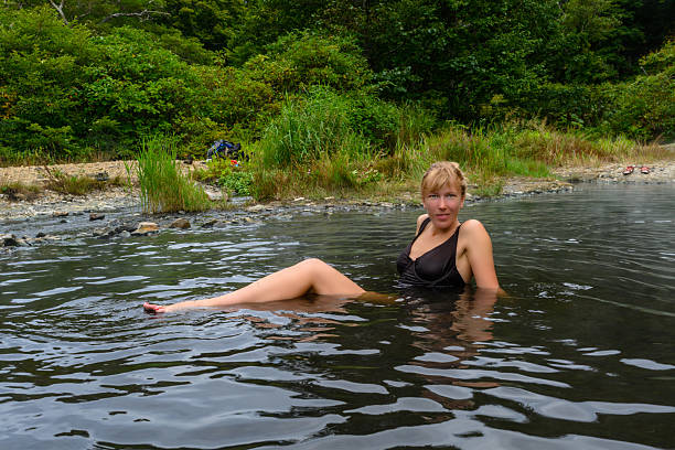 A woman enjoys a peaceful moment while lounging in calm waters, surrounded by lush green trees and a beautiful natural setting, capturing the essence of a summer escape in Russia.
