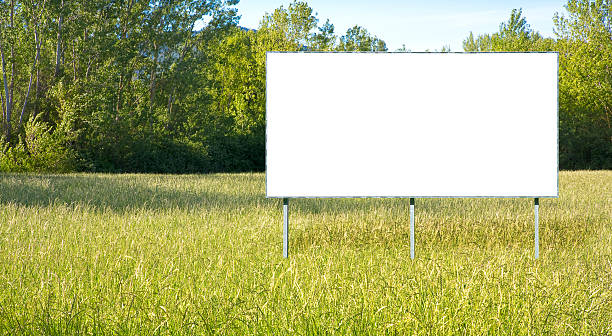 istock Blank advertising signboard in a green field with trees on background - concept with copy space 2245526964
