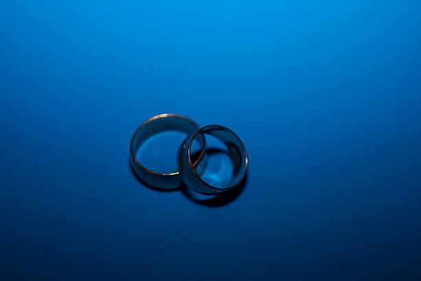 Two classic gold wedding rings are placed together on a deep blue background, illuminated by stark contrast lighting. This minimalist and symbolic image is ideal for themes of wedding, marriage, love, and jewelry.