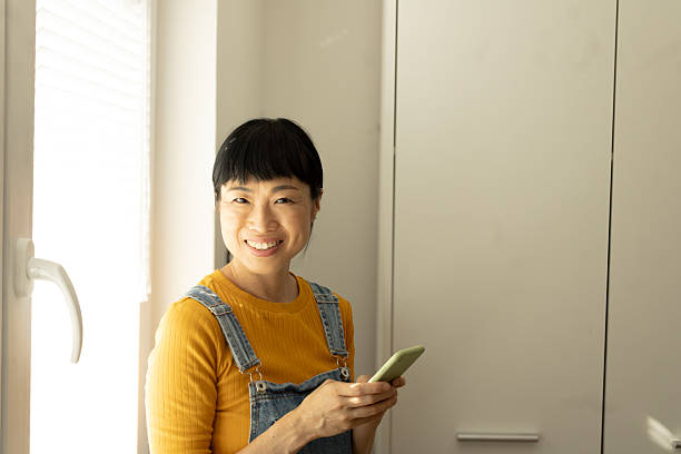 istock Asian woman smiling using smartphone at home 2245529924