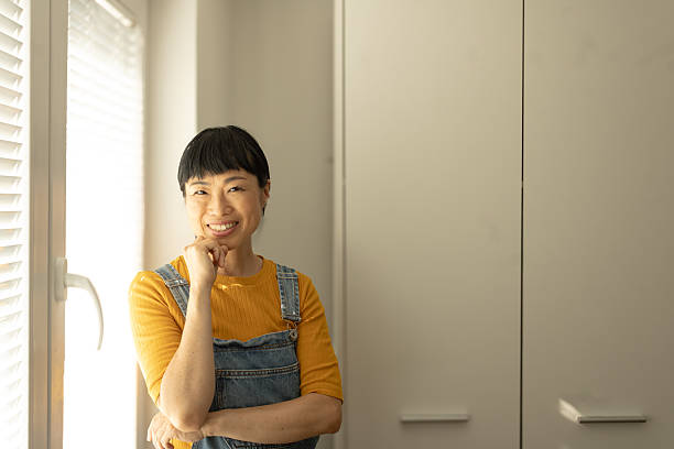 istock Smiling asian woman posing by window in overalls 2245529953