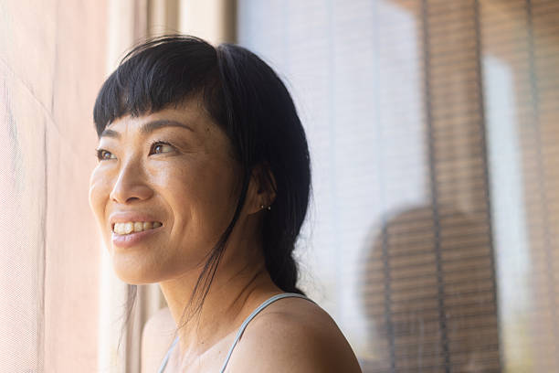 istock Asian woman smiling looking out window feeling hopeful 2245530208