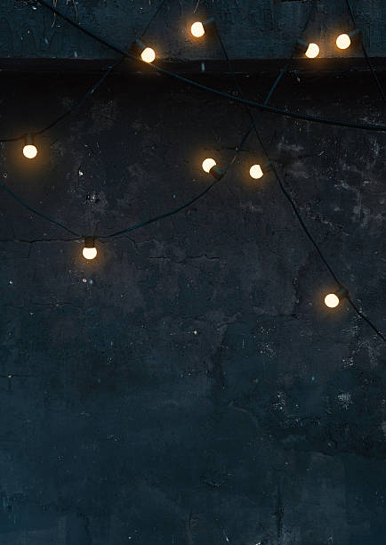 istock Glowing string lights on a dark concrete wall create a moody and cozy ambiance. Industrial textured background perfect for minimalist and trendy designs 2245530586