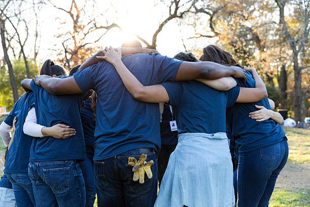 istock Diverse group of people in blue shirts hug outdoors in sunlight, symbolizing teamwork and community spirit. 2245532760