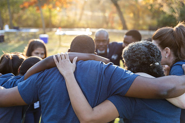 istock A diverse group of people embrace each other outdoors in a team-building exercise during daytime. 2245532761