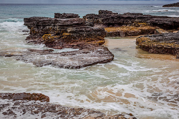 Powerful waves surge over volcanic rocks at Sandy Beach Park, Oahu, with storm clouds gathering over the horizon.
