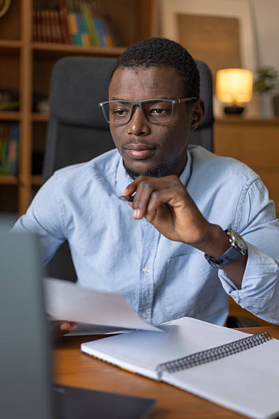 istock African man working from home, focusing on paperwork and laptop 2245534577