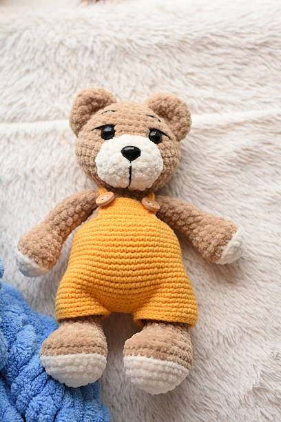 istock Brown knitted bear in yellow overalls 2245539829
