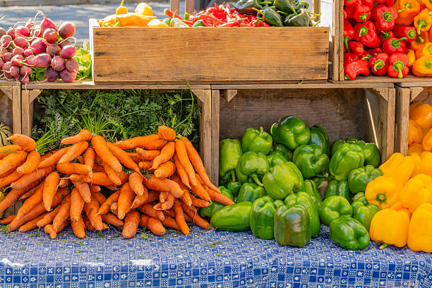 Close up of fresh vegetables on display at an outdoor farmers' market-supermarket including peppers, lettuce and other leafy greens.
