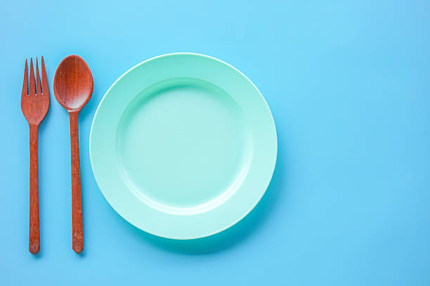 istock Top view of empty green plastic dish and wood spoon and fork on blue background with copy space 2245544332