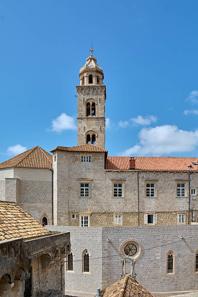 The iconic bell tower of the Franciscan Monastery rises above stone buildings and terracotta roofs in Dubrovniks Old Town, a UNESCO heritage site.