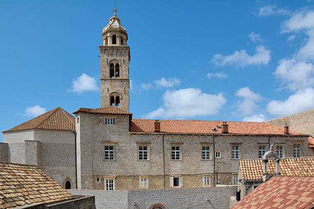 View of medieval architecture in Dubrovnik, Croatia. Historic stone buildings and a bell tower set against a blue summer sky on the Dalmatian coast.