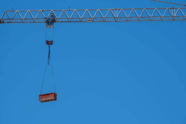 Construction crane lifting red cargo against blue sky in urban setting.