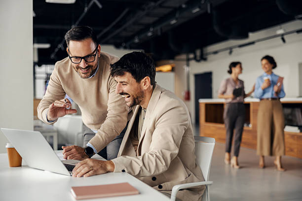 istock Businessmen collaborating on laptop in modern office laughing 2245557779