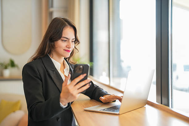 istock Smiling businesswoman using smartphone and laptop in modern office 2245558908