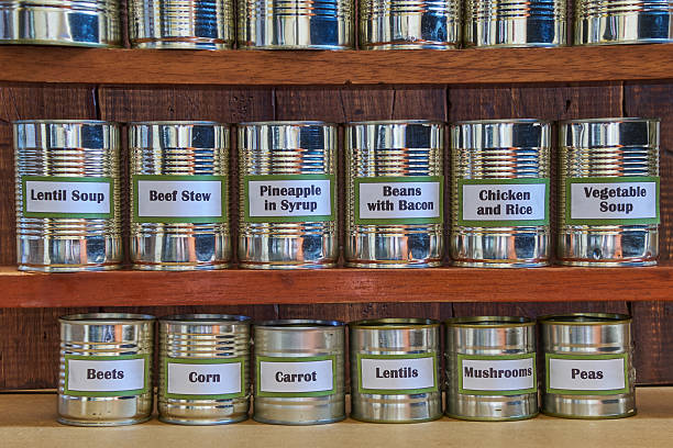 Open cans of beans, mushrooms, carrots, corn, peas, green beans, lentils, asparagus, and olives on a white background with copy space.