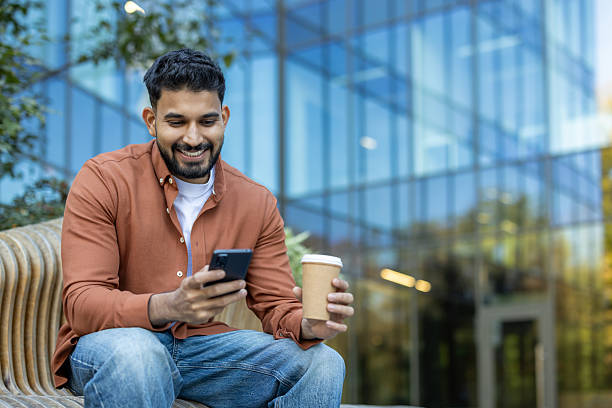 istock Man Relaxing Outside a Modern Building Using Smartphone and Holding Coffee Cup 2245562237