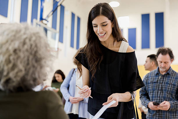 istock Young woman smiling while holding papers and pencil in a line 2245563873