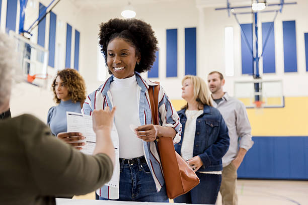 istock Diverse group of people lining up and smiling at a community event, possibly a voting precinct. 2245563884