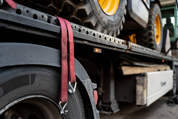 istock Transport truck with heavy machinery secured on trailer using red straps, representing mechanical fastening system, logistics process and industrial equipment delivery for construction operations 2245564473