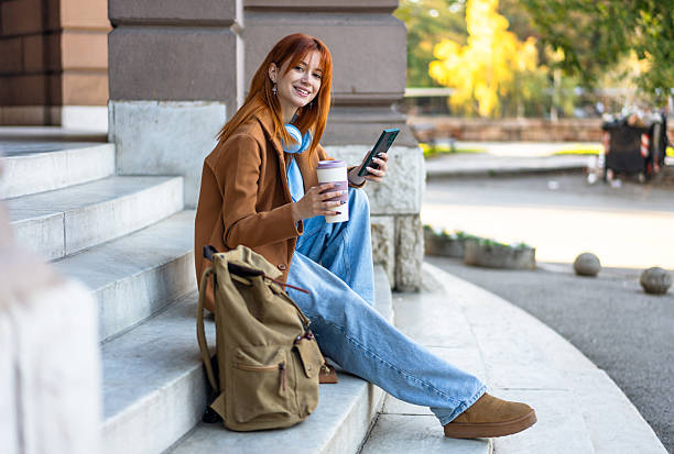 istock Young woman drinking coffee holding phone on steps 2245569749