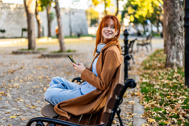 istock Young woman relaxing on park bench, using smartphone 2245570404