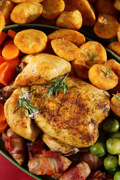 istock Full frame image Sunday roast dinner with all the trimmings on green serving dish, whole roast chicken with crispy, golden skin garnished with Rosemary sprigs, surrounded by side dishes of Brussel sprouts, roast potatoes, sliced carrots, pigs in blankets 2245573289