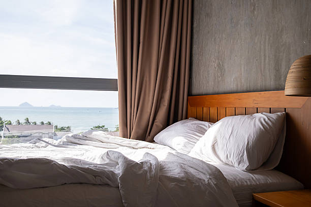 istock Cozy bed with white sheets and pillow in sunlit room by large window overlooking the sea 2245582761