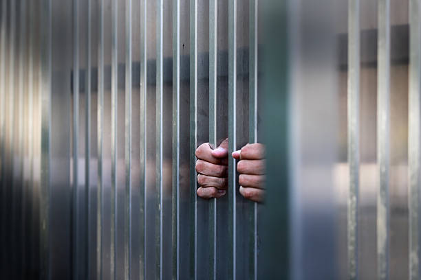 istock Hands Grasping Metal Bars of Prison Cell in Locked Up Scenario 2245589843