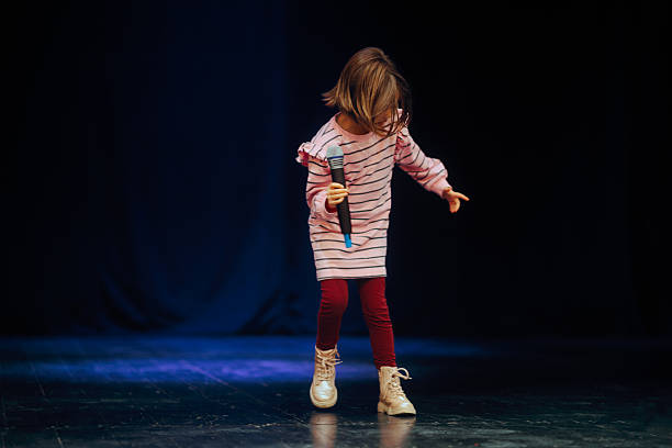 istock Little Girl Dancing on a Stage Holding the Microphone 2245594649
