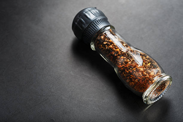 Peppercorns cumin and salt in a transparent mill on a black background