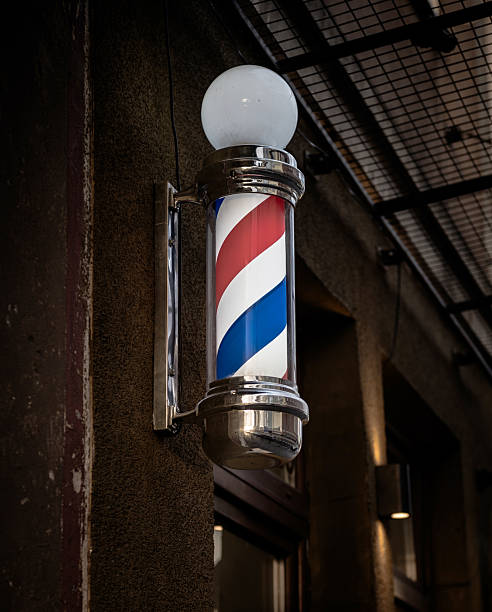 istock Traditional barber pole with blue red white stripes mounted outdoors on wall of classic barbershop for business advertisement and retro style 2245601310