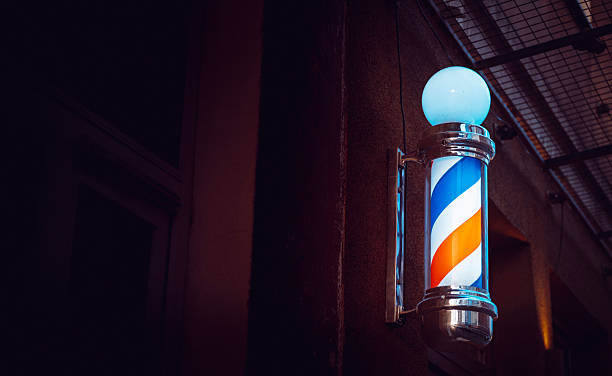 istock Classic barber pole with red white blue spiral stripes mounted on building exterior as iconic barbershop sign for traditional hair salon 2245601319