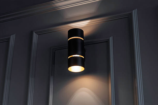 Modern black wall sconce emits soft light on a textured gray wall, creating a cozy, stylish ambiance with gentle upward and downward illumination.