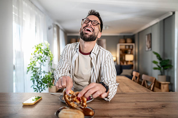 istock Young man laughing and eating pretzel at home 2245614969