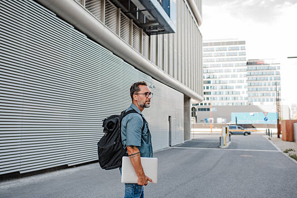 Handsome man with tattoos with laptop under arm, heading to office, studio.
