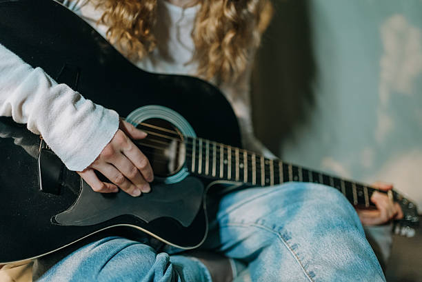 istock Young woman's delicate fingers strumming black acoustic guitar strings, creating soft musical notes in warm, intimate home setting 2245622833