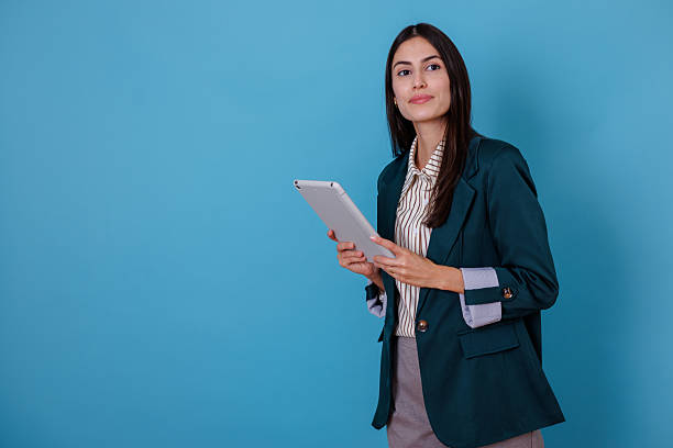 istock Businesswoman holding tablet computer on blue background, looking confident and focused for digital tasks 2245624536