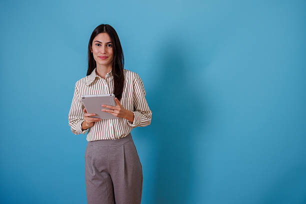 istock Professional woman using digital tablet, smiling at camera, with copy space on bright blue background 2245627045