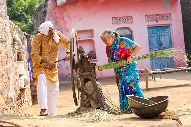 Old indian farmers couple using grass cutting machine at home.