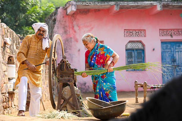 Old indian farmers couple using grass cutting machine at home.