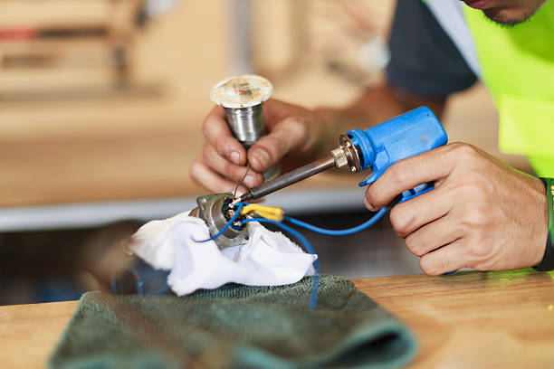 Teamwork engineering maintenance industrial technology safety management electrician soldering wiring repair hands tool bench focused technician performing precise solder joint electrical