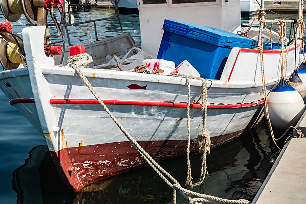 Weathered fishing trawler and modern boat docked in a scenic Mediterranean port on a sunny day
