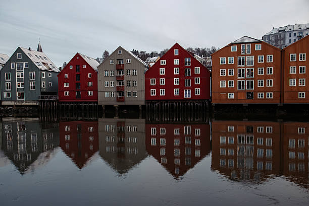 Row of traditional colorful wooden wharves or warehouses (called 'Brygge') on wooden stilts reflected perfectly in the Nidelva River in Trondheim, Norway.