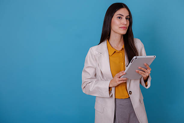 istock Confident businesswoman holding tablet on blue background, representing technology and professional success 2245633479